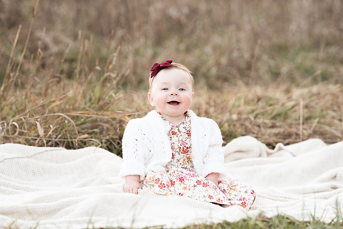baby girl in floral dress sits on blanket in brown field