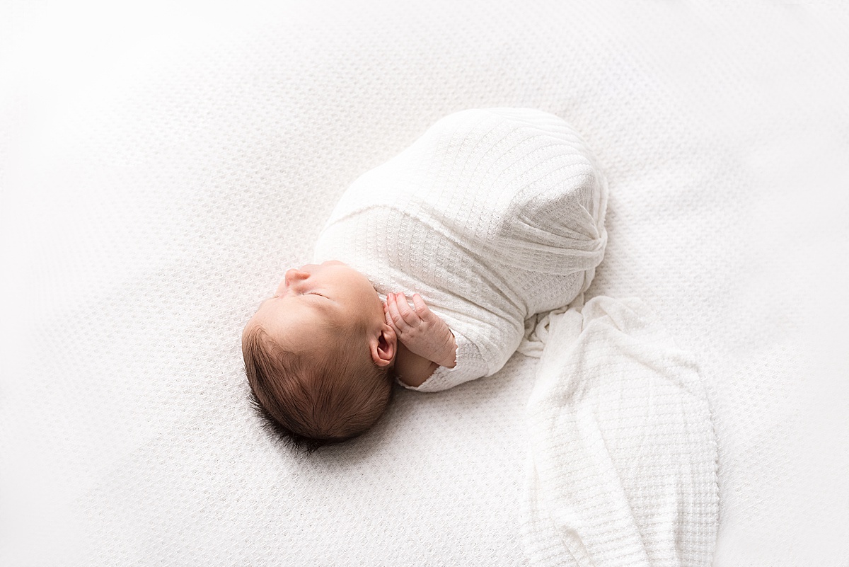 photography newborn baby boy snuggled up in white swaddle