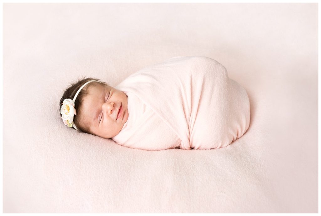 newborn girl wrapped in peach sleeps with flower headband