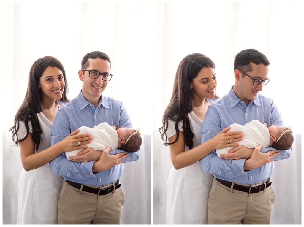 mom and dad hold newborn girl in front of studio window