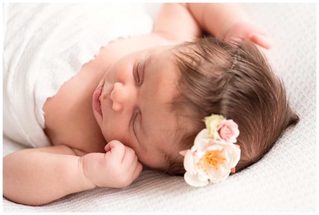 newborn girl with floral headband lightly wrapped in white sleeps