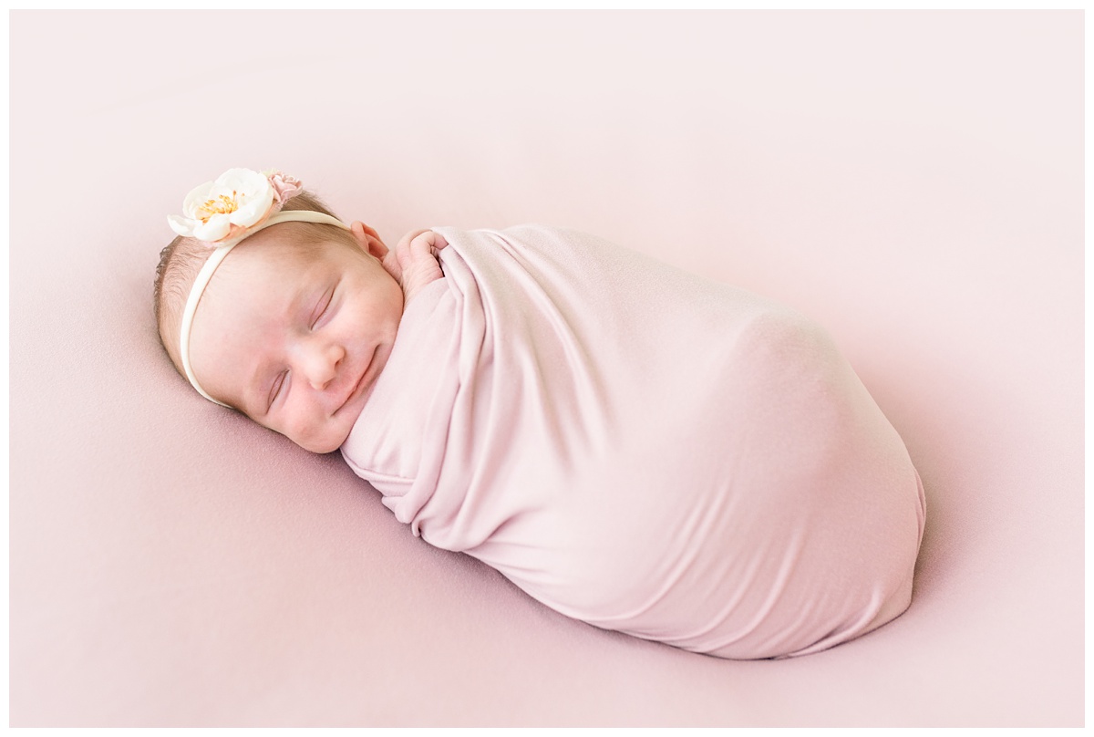 studio newborn girl in light pink wrap smiles and sleeps