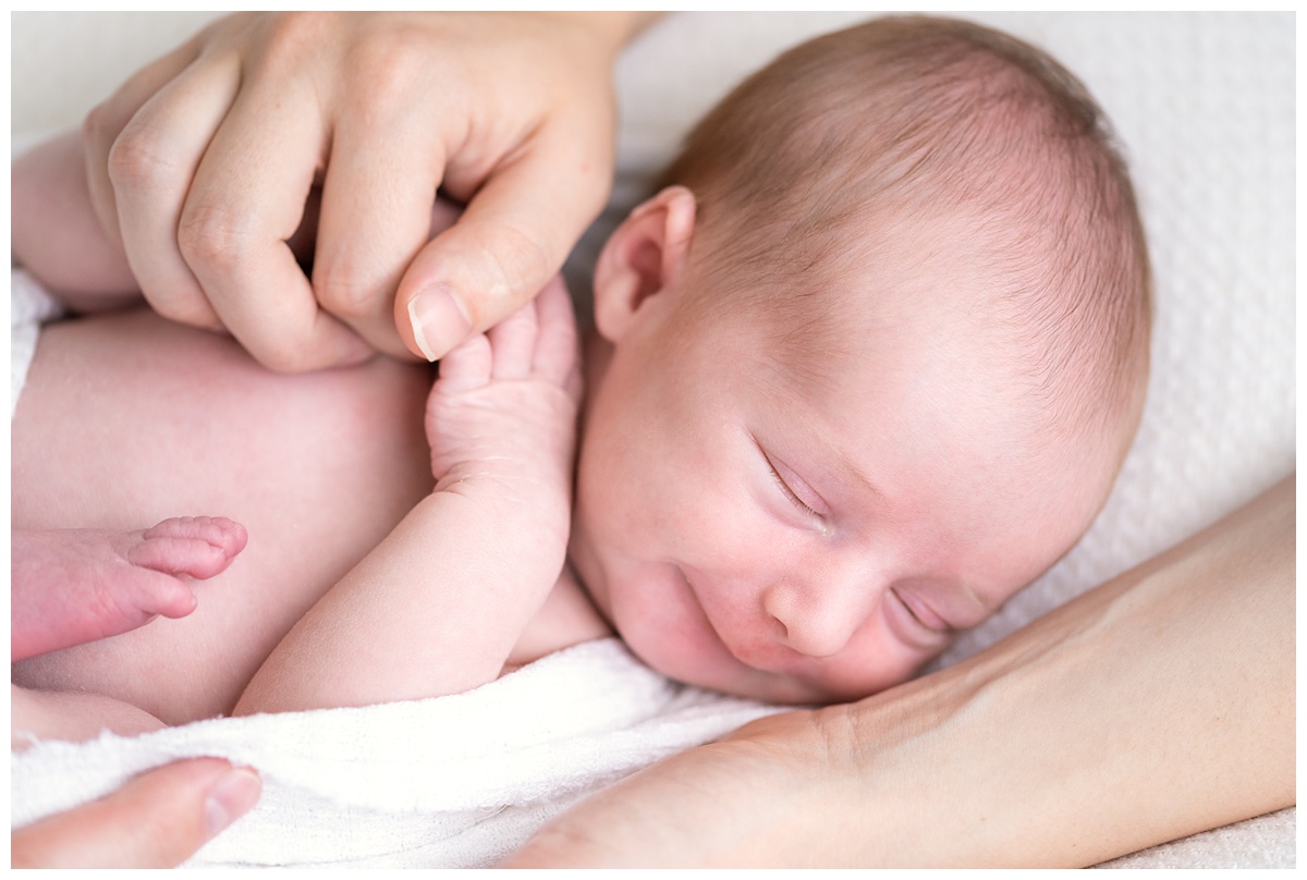 newborn girl smiles while grasping moms fingers