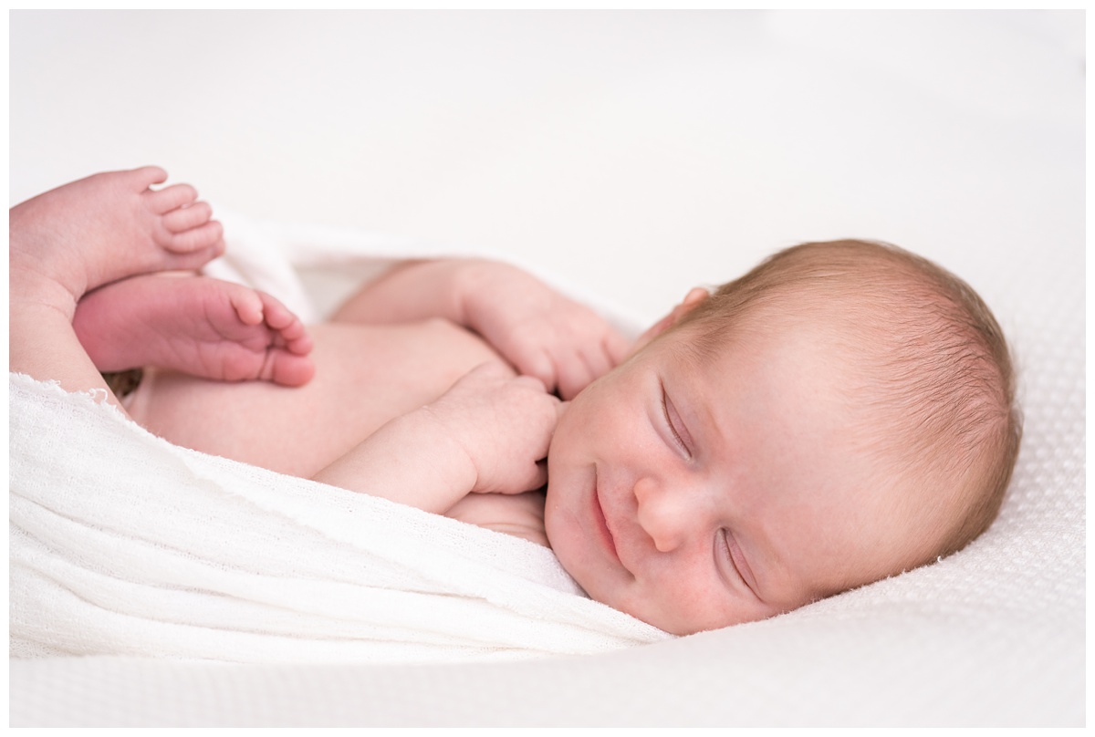 newborn girl smiles while she sleeps with white wrap
