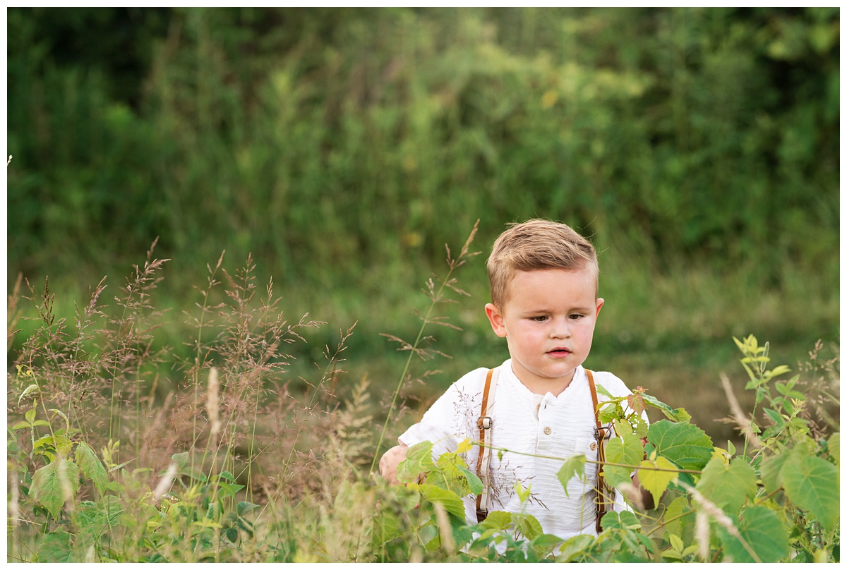 toddler boy wearing zara kids shirt and suspenders plays in field