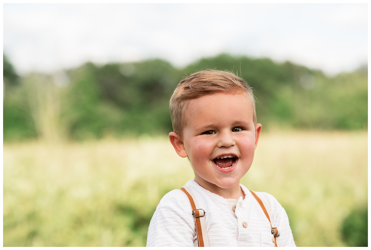 toddler big brother smiles wide outside in field during maternity session