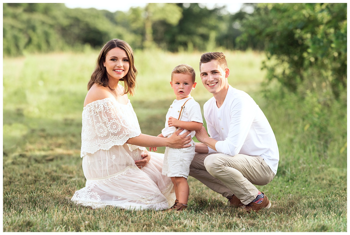 mom toddler and dad sit in field for their summer maternity session