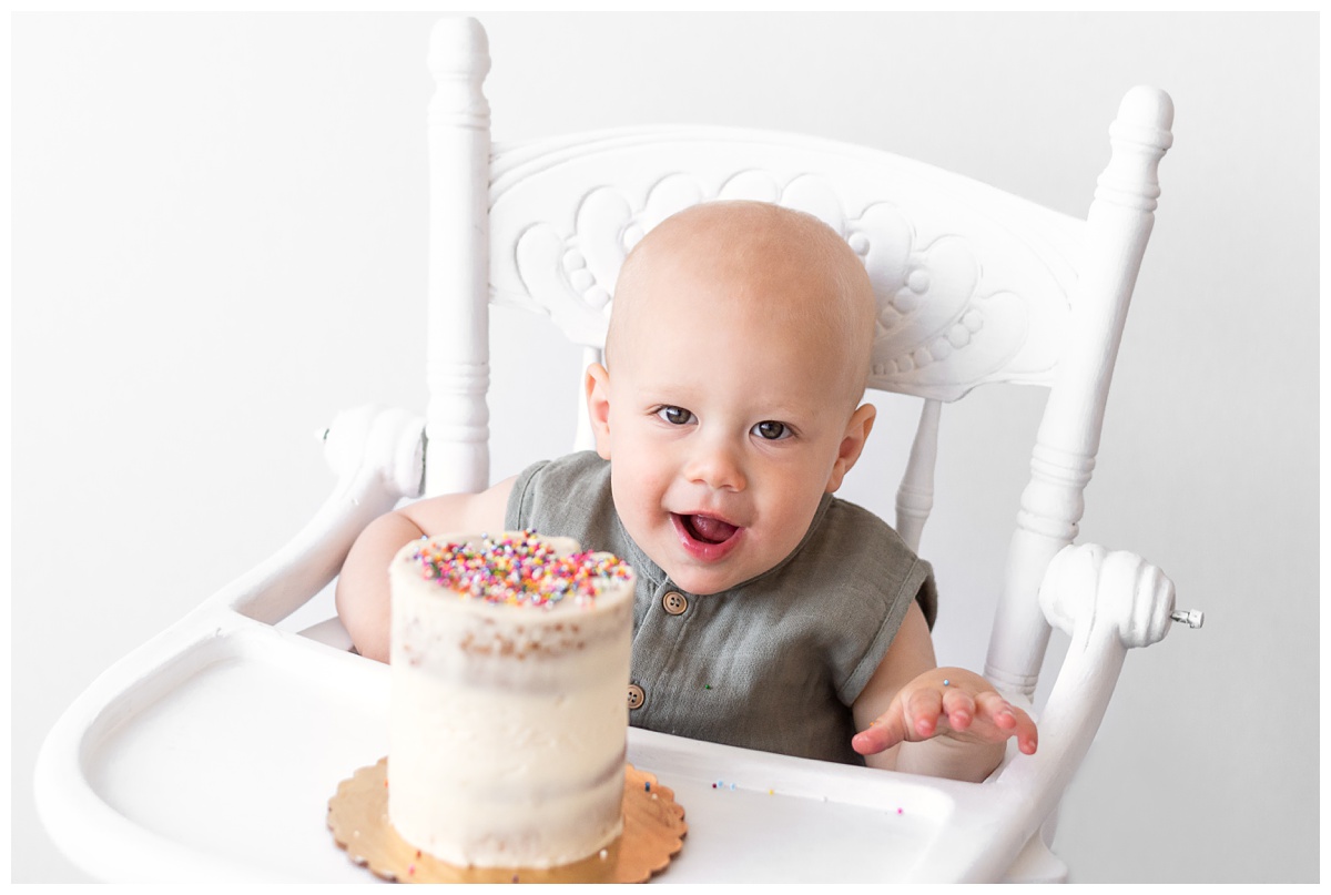 baby boy in green romper with cake in highchair