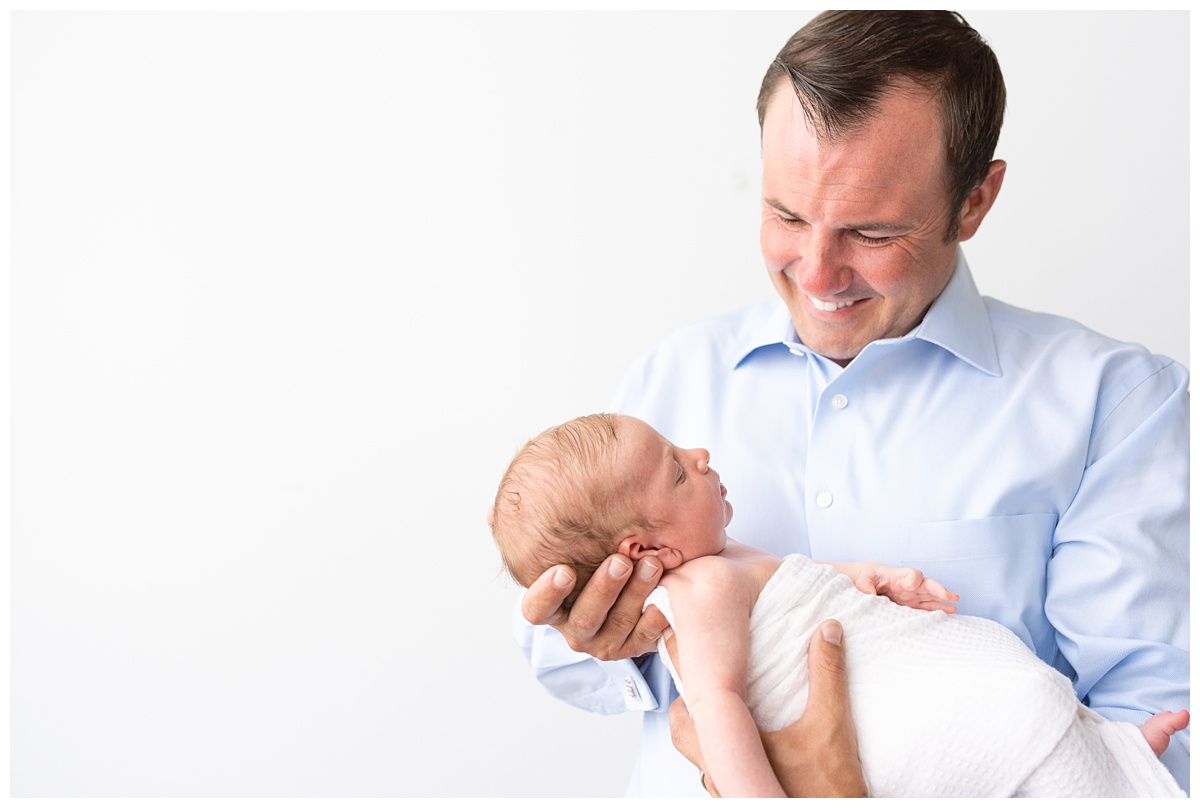 dad smiles in blue shirt down at son in studio newborn session columbus