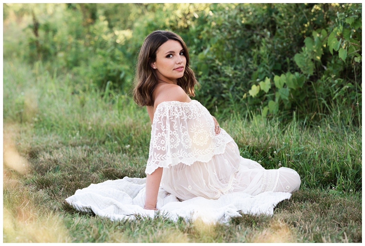Top maternity Photographer Columbus Ohio mother cradles belly sitting in field in lace dress