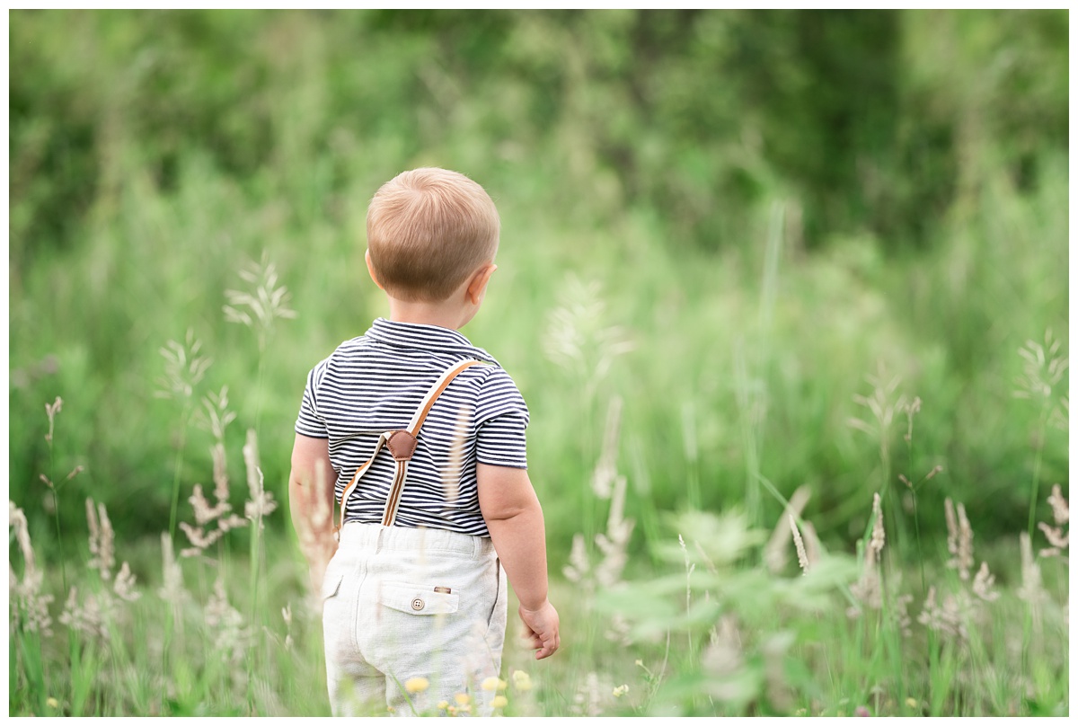 Top baby Photographer Columbus Ohio toddler boy walks in field with suspenders