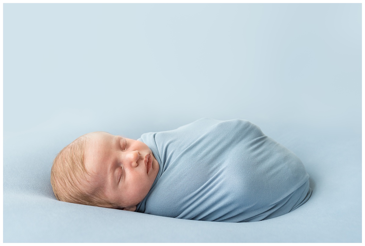 Top Newborn Photographer Columbus Ohio baby boy wrapped in blue sleeps in studio