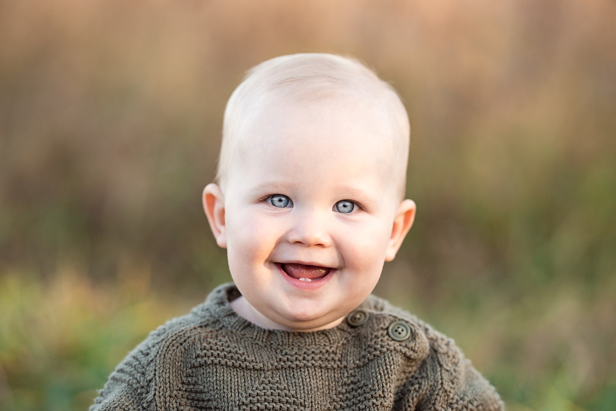 columbus baby photographer toddler boy in green sweater grins in field 