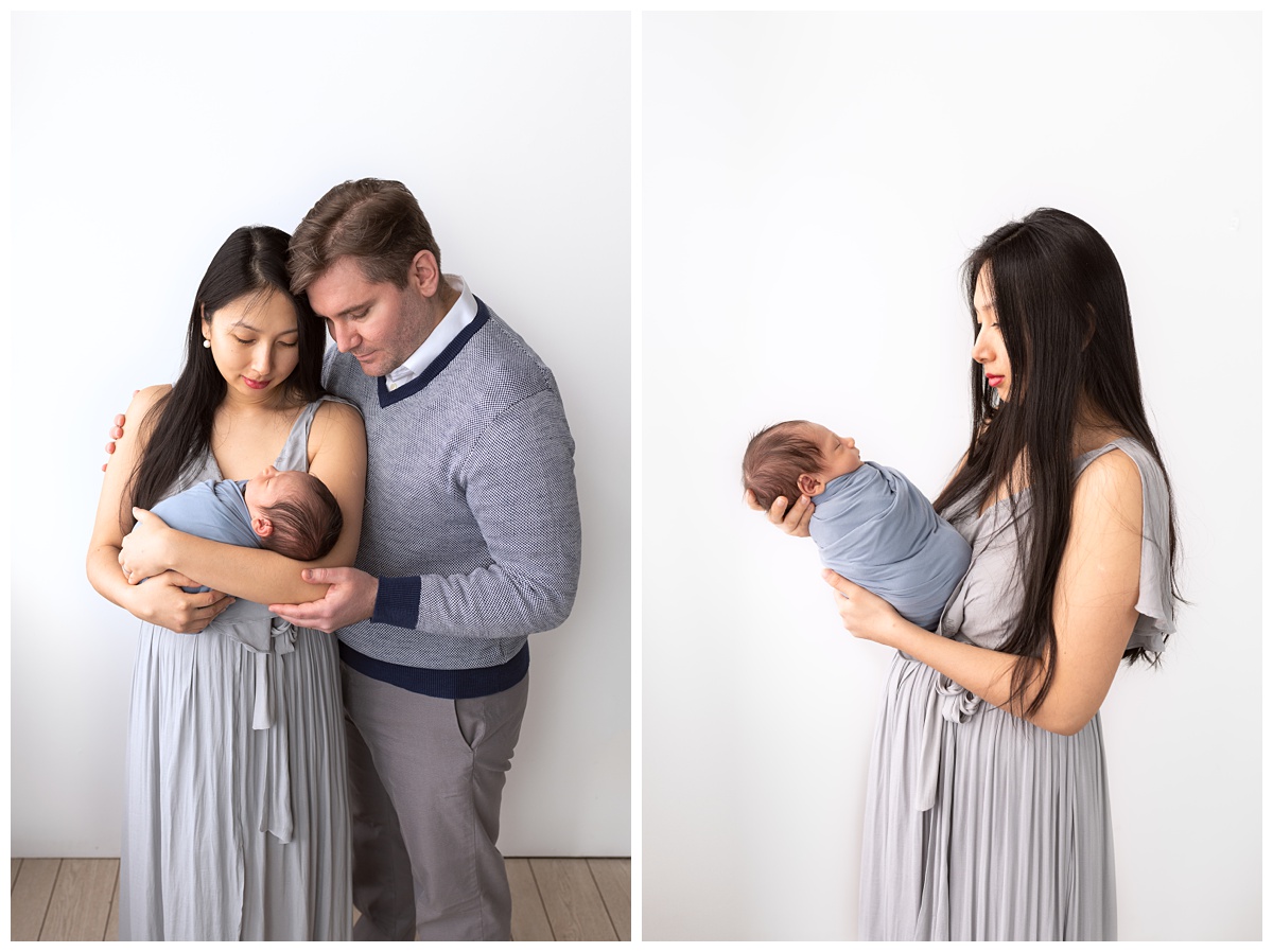 Best Columbus Newborn Photographer mom in blue dress holds newborn in blue wrap with dad in blue sweater hugging them 