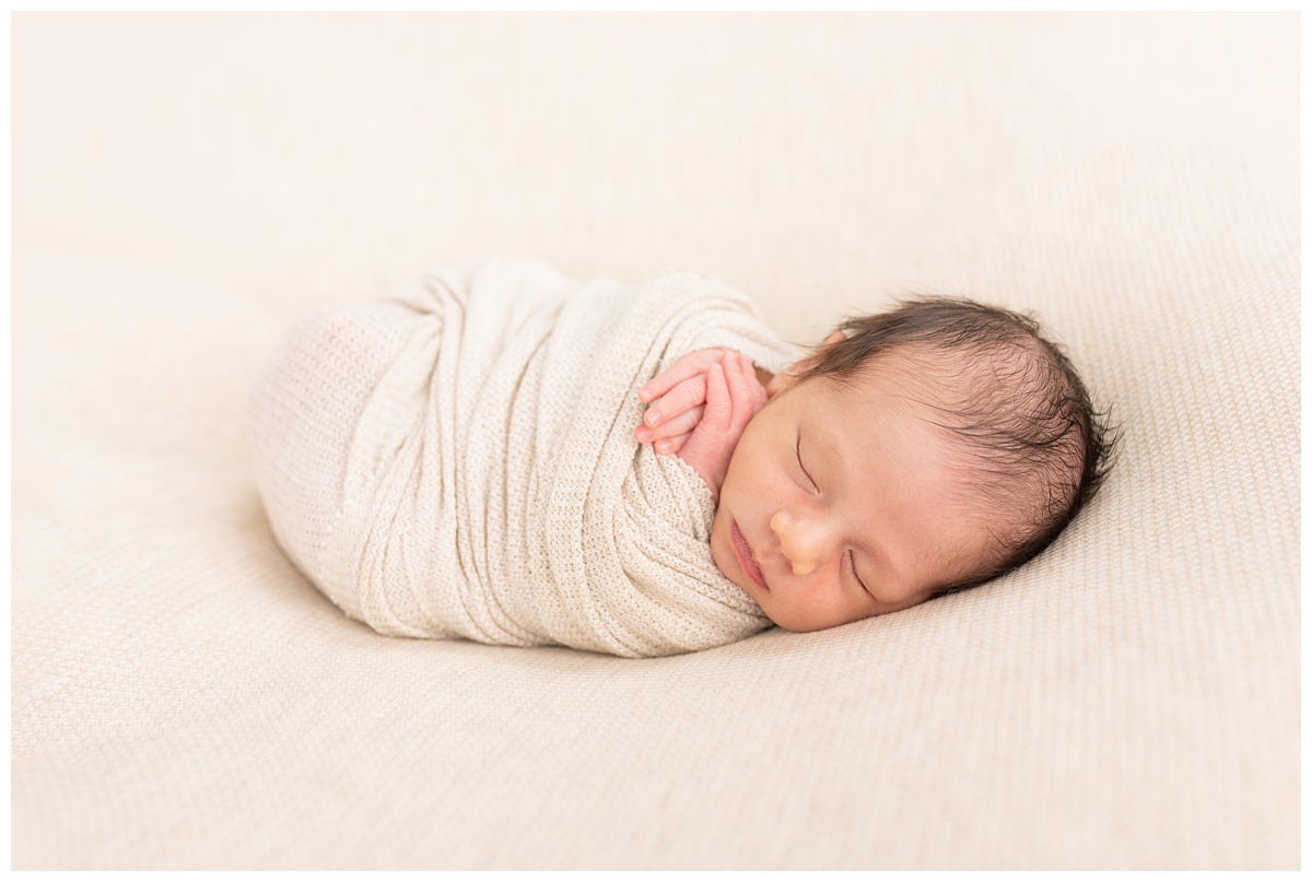 Best Columbus Newborn Photographer newborn boy sleeps with hands folded and cream wrap 
