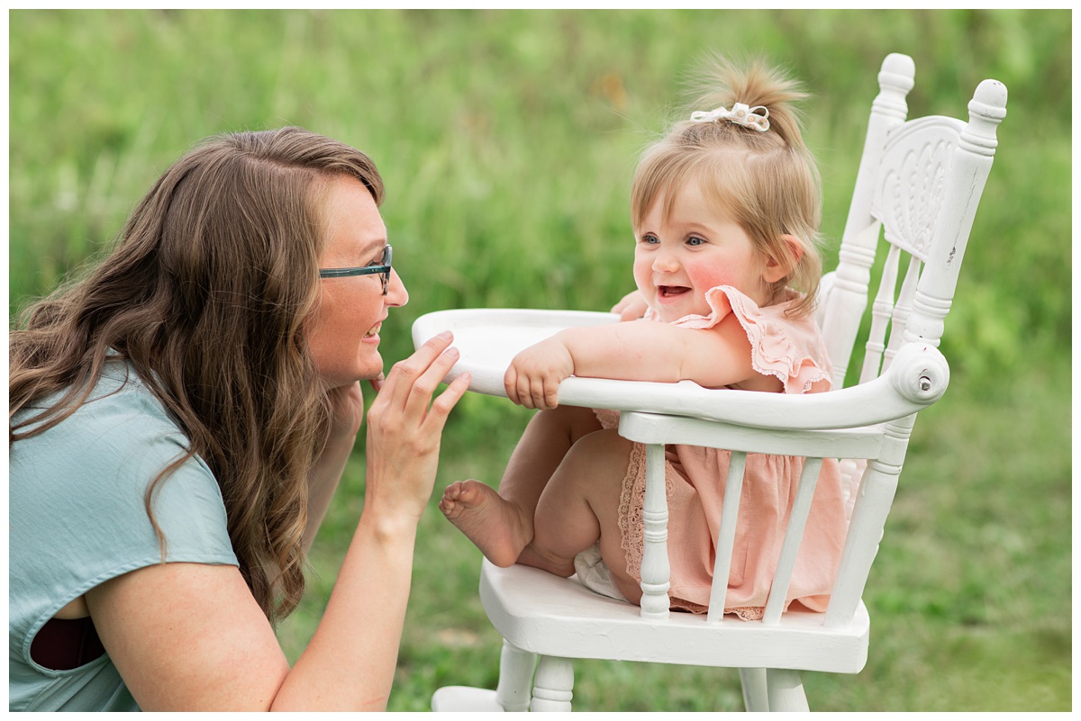Family Photographers Columbus  baby girl in pink dress sits on white highchair with mom in blue dress outside