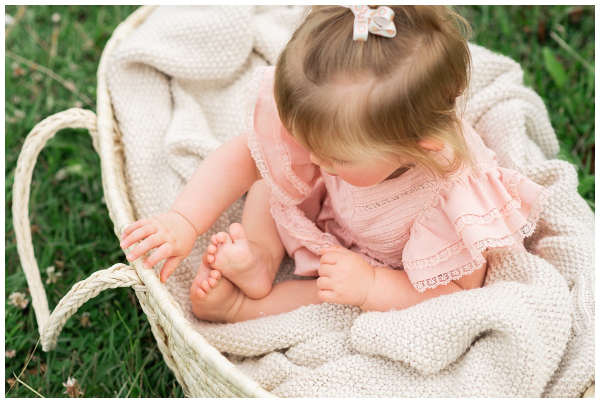 Family Photographers Columbus girl in pink dress sits in moses basket outside