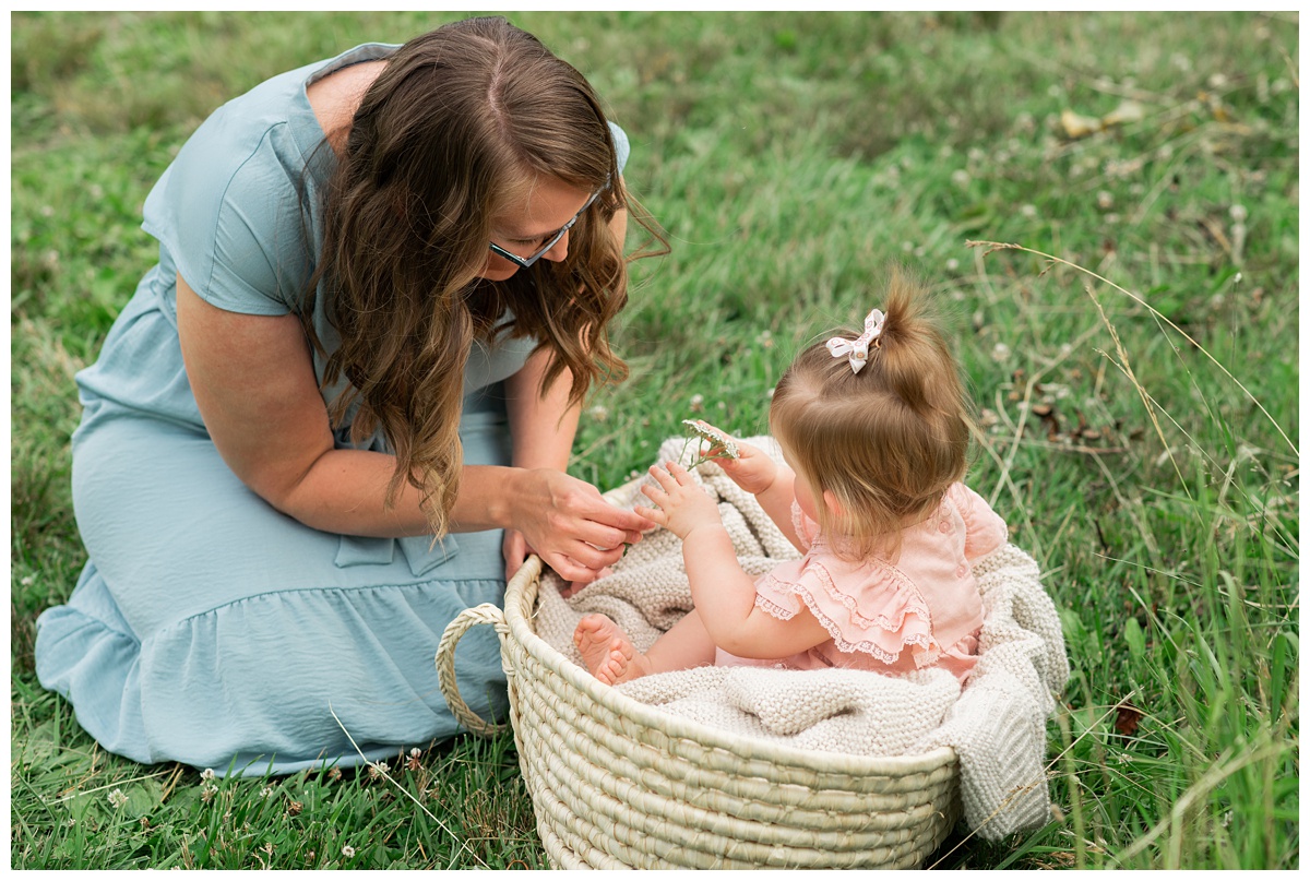 Family Photographers Columbus baby girl in pink dress sits in moses basket next to mom in blue dress