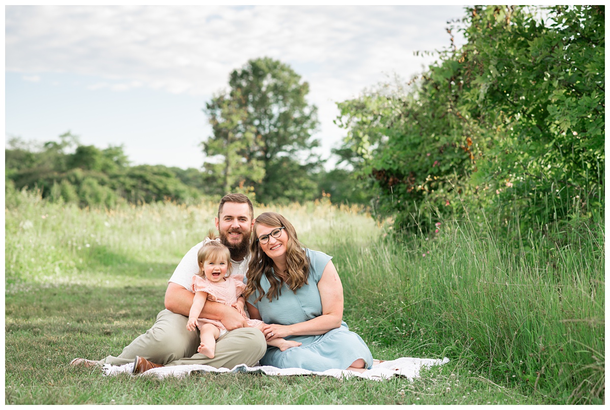 Family Photographers Columbus Ohio Summer 2021 family of three sit outside on grey blanket in green field