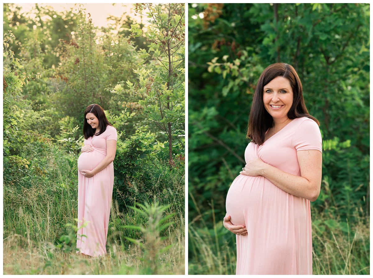 best maternity photographer mom in pink dress stands holding belly in green field 