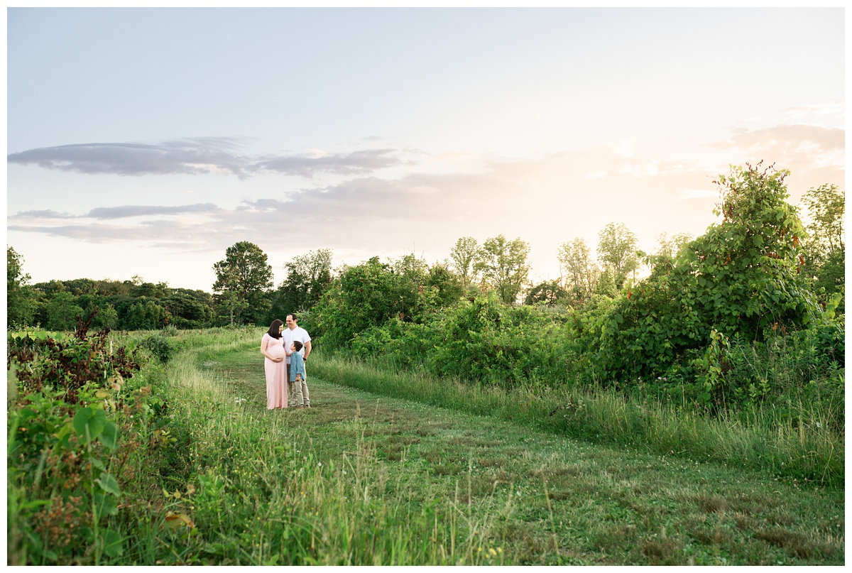 best maternity photographer family of three hug each other in green field at sunset