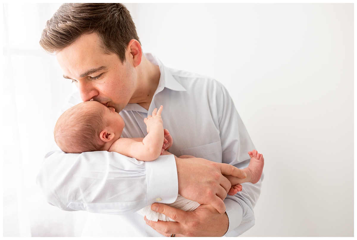 neutral newborn session Columbus dad in blue shirt kisses newborn boy in white studio