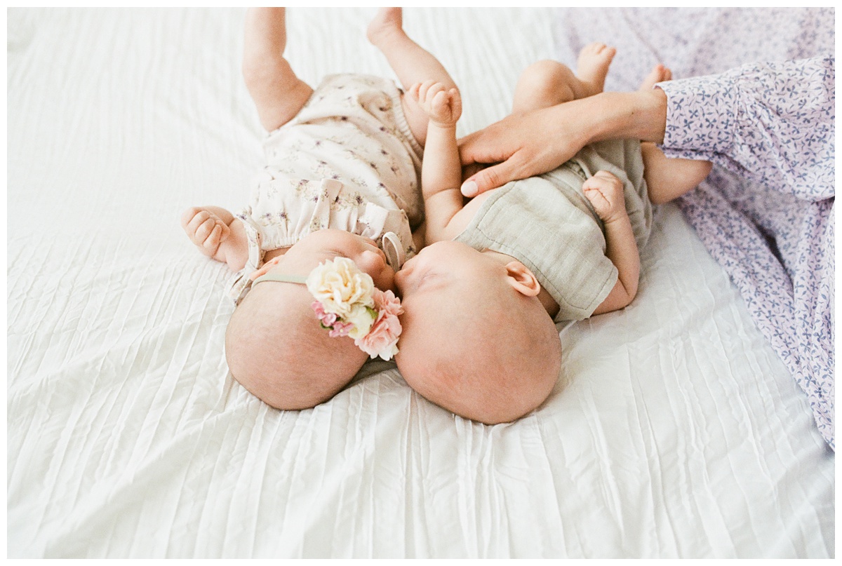 Professional Baby Photographer Columbus Ohio twins snuggle heads together on white bed with floral jumper and headband