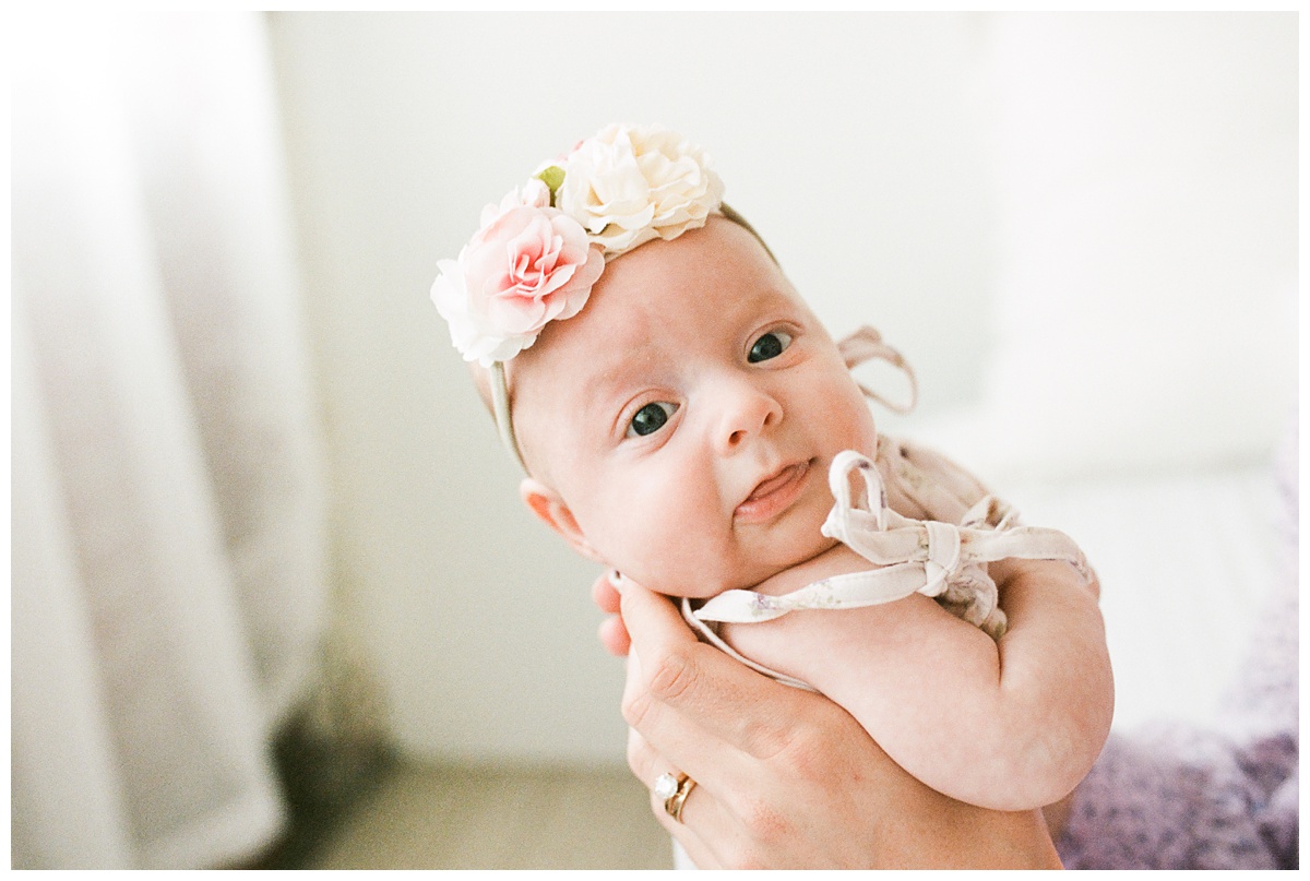 Professional Baby Photographer Columbus Ohio little three month old girl with floral headband smiles at camera in moms arms