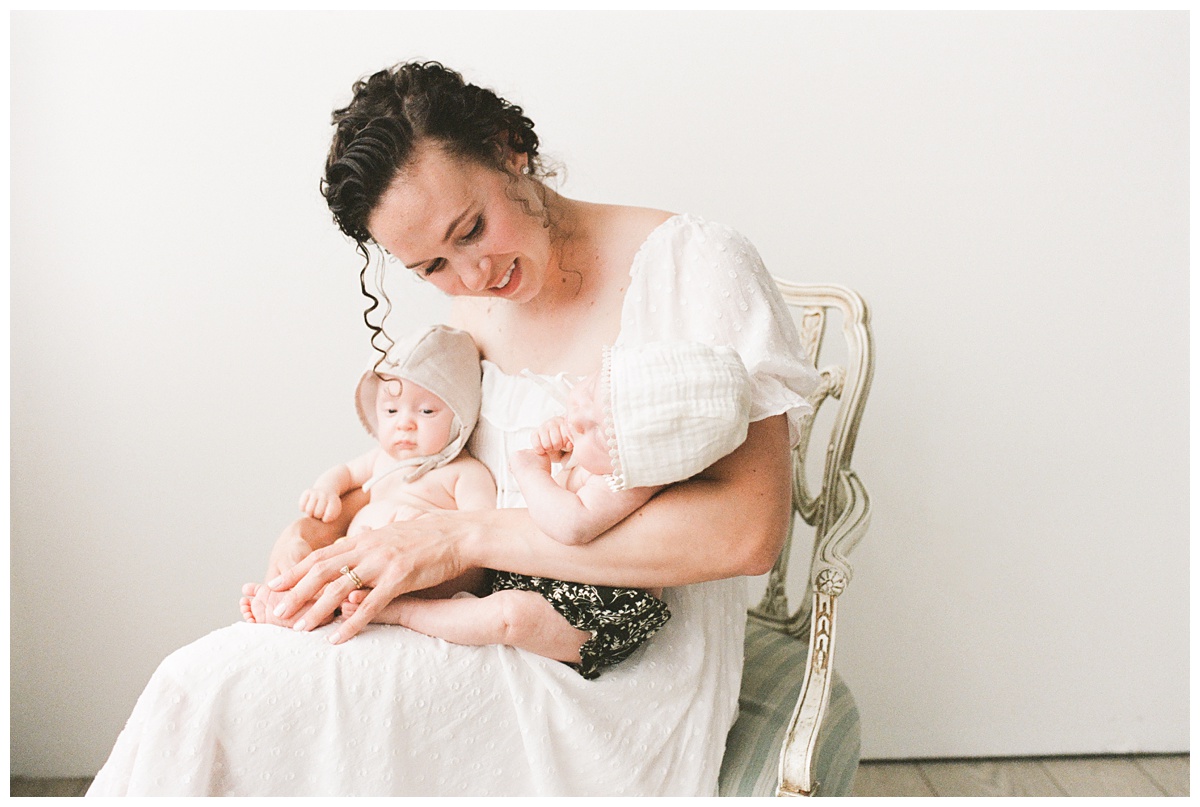 Professional Baby Photographer Columbus Ohio mom in white dress holds her twins seated in white studio