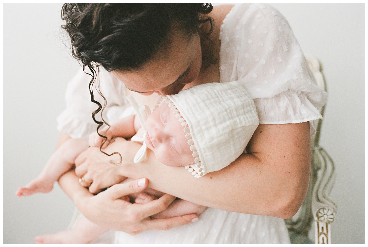 Professional Baby Photographer Columbus Ohio mom in white dress nuzzles baby in white bonnet 