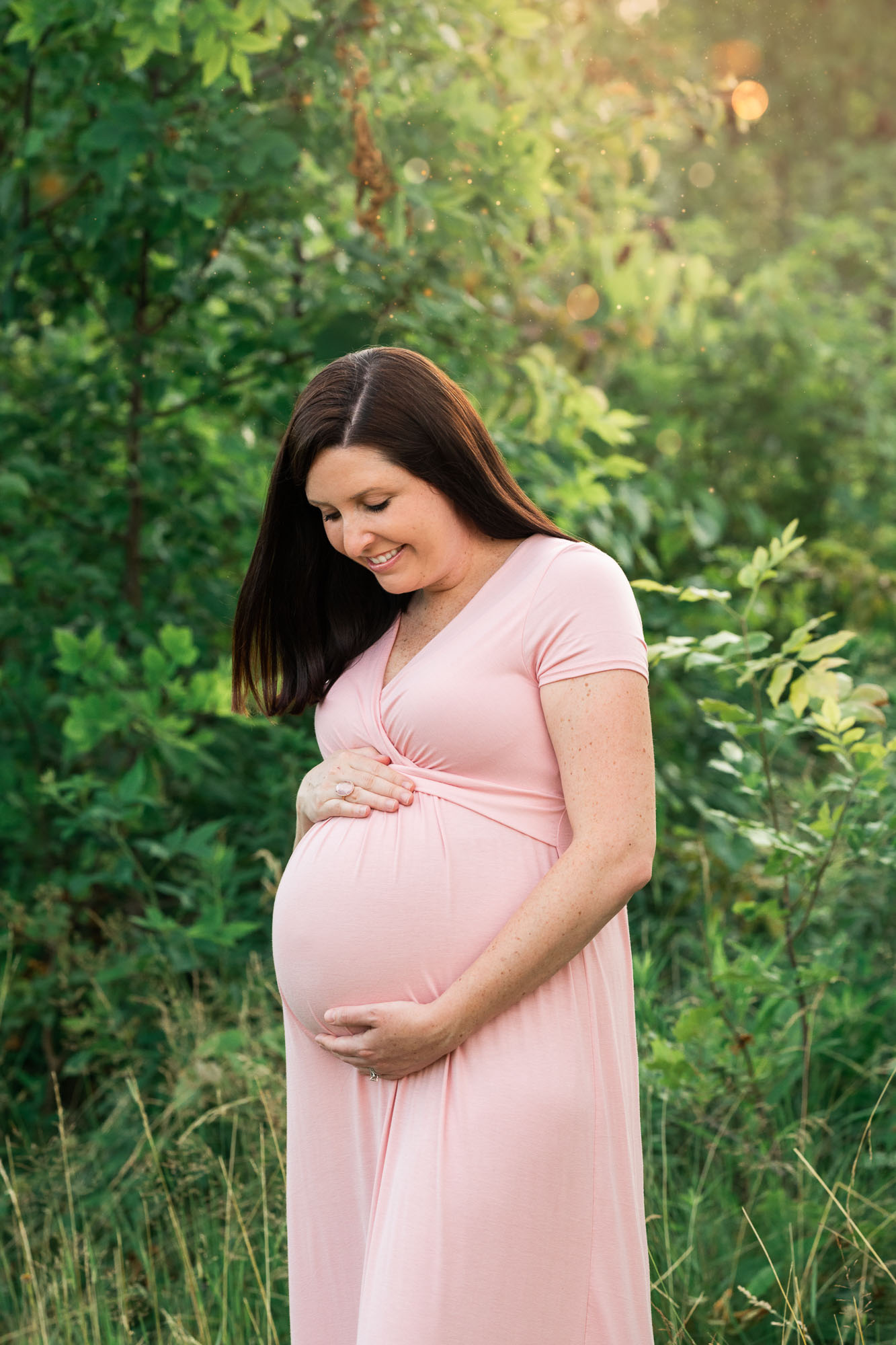best maternity photographer mom in pink dress holds her pregnant belly in green field