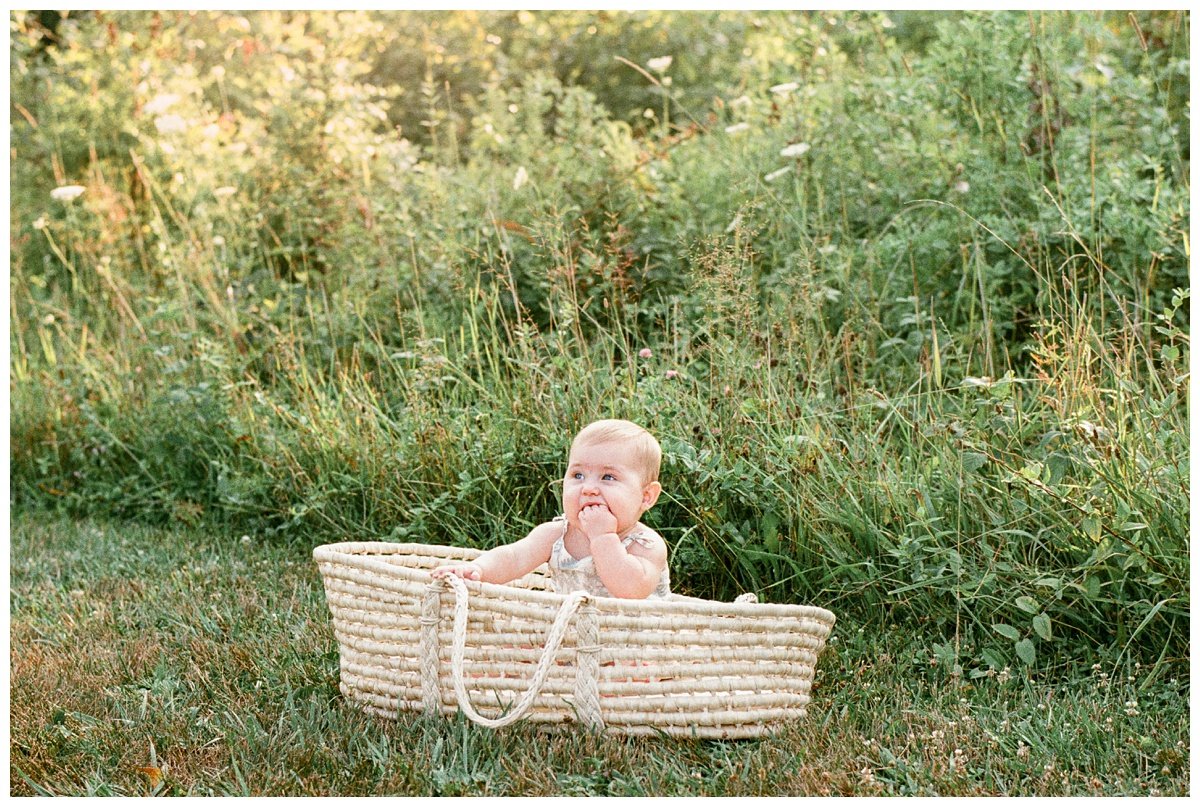 baby girl in moses basket in field eats her hand