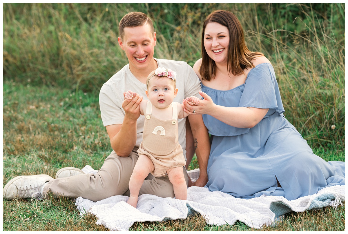 Summer field milestone session baby girl in rainbow onesie with parents