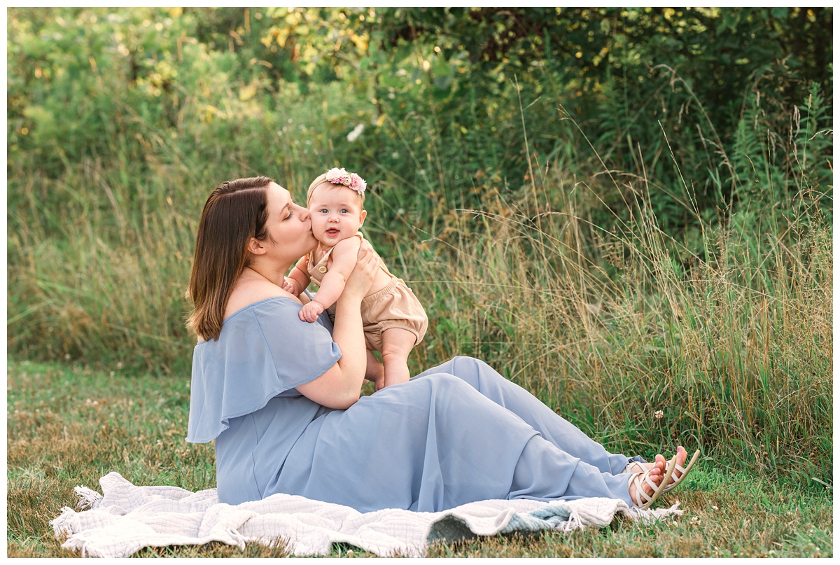 mom kisses six month old daughter in green field