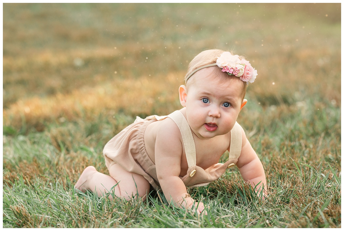 baby girl with flower headband crawls in grass