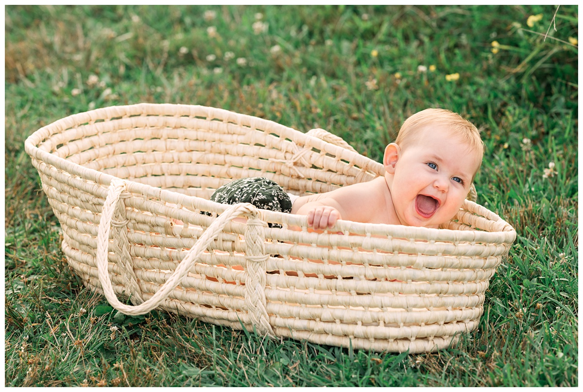 little girl plays in moses basket Summer field milestone session