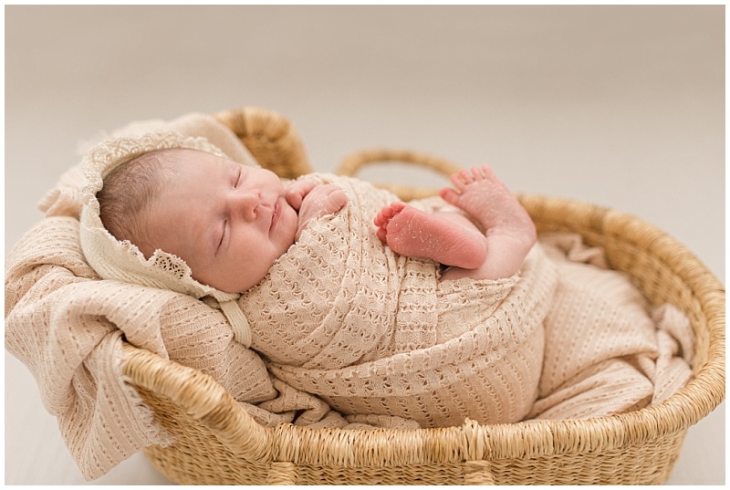 newborn girl in moses basket wearing tan bonnet