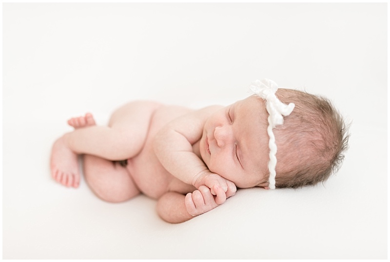 newborn girl with white bow sleeps on side in white background